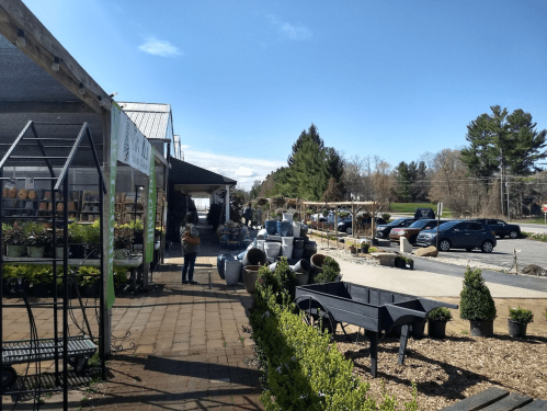 A garden center with plants, pots, and customers browsing under a clear blue sky.