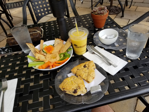 A table set with a plate of hummus and veggies, two scones, a smoothie, and glasses of water.