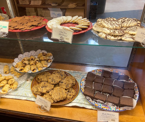 A display case filled with various baked goods, including cookies, brownies, and pastries, labeled with names.