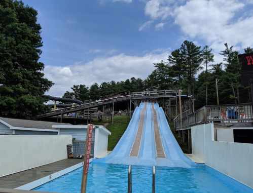 A water slide at a park, with a clear blue sky and trees in the background. The slide leads into a pool.