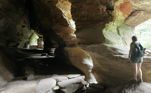 A person stands in a rocky cave, surrounded by colorful stone formations and natural light filtering in.