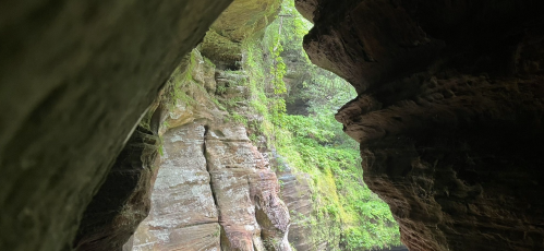 A view through a rocky archway, revealing lush greenery and steep cliffs in a natural setting.