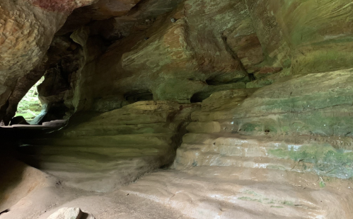 A rocky cave interior with layered green and brown stone formations and soft lighting.