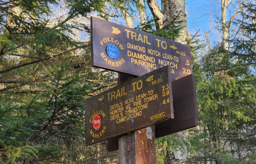 Wooden trail sign with directions and distances to various locations, surrounded by trees in a forested area.