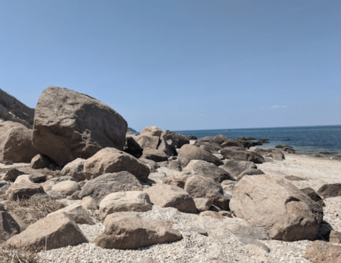 Rocky shoreline with large boulders and calm blue water under a clear sky.