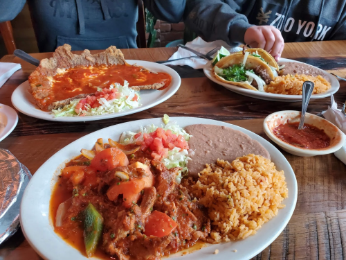 A table with three plates of Mexican food: rice, beans, tacos, and a breaded dish with sauce and salad.