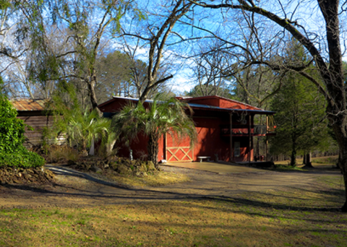 A red barn surrounded by trees and a grassy area under a clear blue sky.