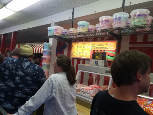 A busy ice cream shop with colorful tubs on shelves and customers waiting in line to order.