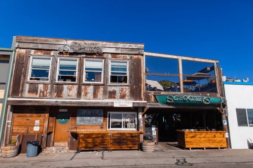 A rustic wooden building with large windows, featuring a sign that reads "Schooners," under a clear blue sky.