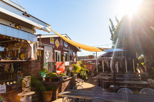 A sunny outdoor dining area with rustic decor, tables, and colorful signage at a casual restaurant.