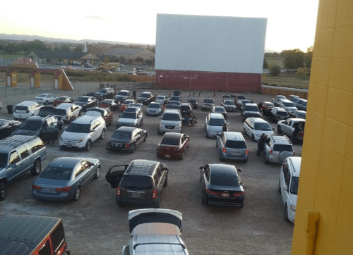 Aerial view of a crowded drive-in movie theater parking lot filled with cars, with a large screen in the background.