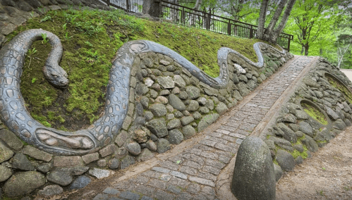 A stone pathway alongside a moss-covered hill featuring a carved snake design integrated into the landscape.
