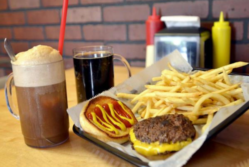 A tray with a cheeseburger, fries, a hot dog with mustard and ketchup, and two drinks: a soda and a root beer float.