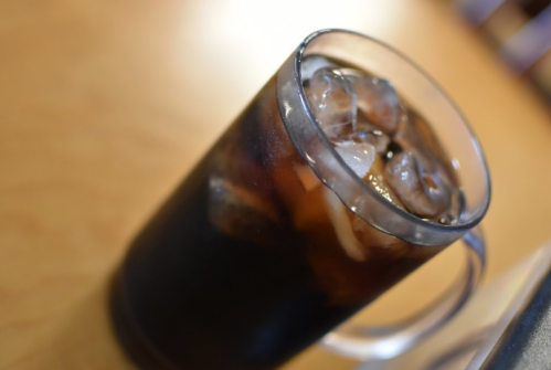 A glass of iced coffee with ice cubes, sitting on a wooden table.
