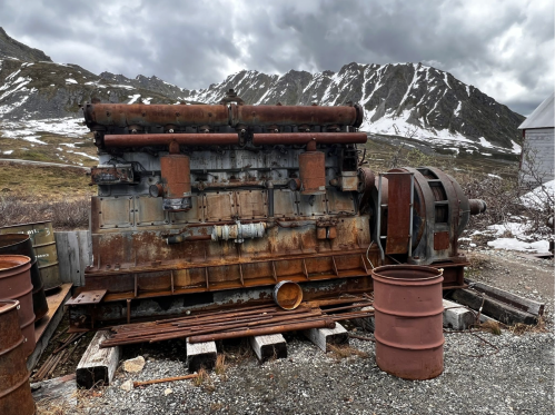 Rusty industrial machinery sits in a barren landscape with mountains and snow in the background.