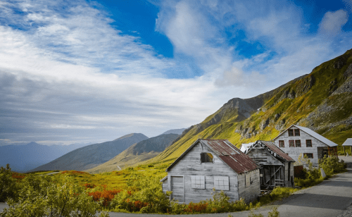 A scenic view of mountains and colorful foliage, featuring old wooden buildings in a rural landscape.