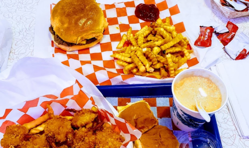 A tray with a burger, crinkle-cut fries, chicken tenders, and a drink, all served with ketchup packets.