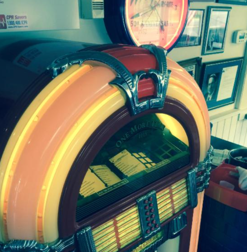 A vintage jukebox with a colorful design, displaying the title "One More Time" and surrounded by framed pictures.