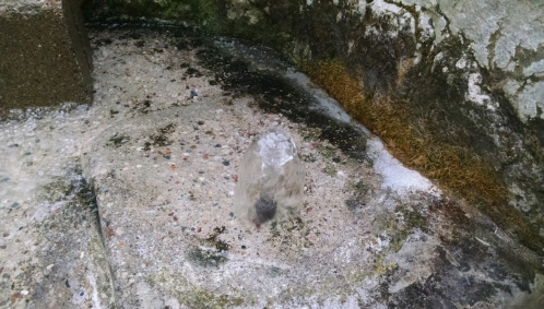 A small ice formation on a rocky surface, surrounded by patches of frost and debris.