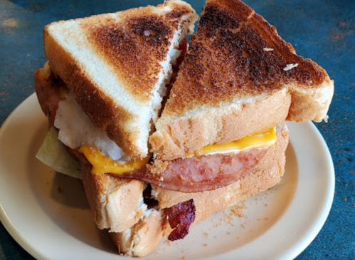 A stacked sandwich with toasted bread, layers of cheese, ham, and lettuce, cut into quarters on a plate.