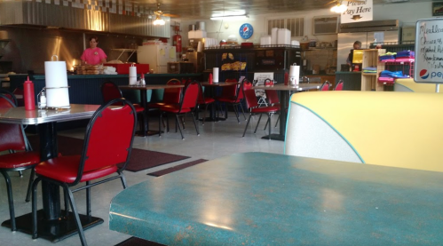 A diner interior with red chairs, teal tables, and a counter in the background. A staff member is visible.