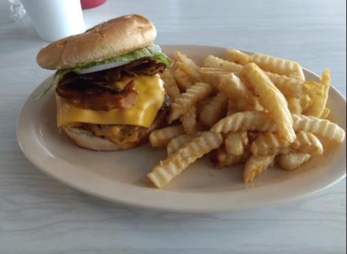 A cheeseburger with bacon, lettuce, and pickles, served with a side of crinkle-cut fries on a plate.