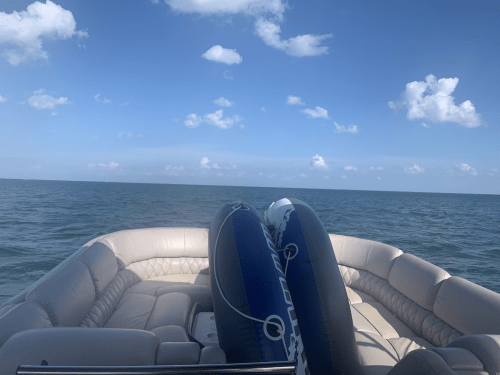 View from a boat with two inflatable tubes, overlooking calm waters and a clear blue sky with scattered clouds.