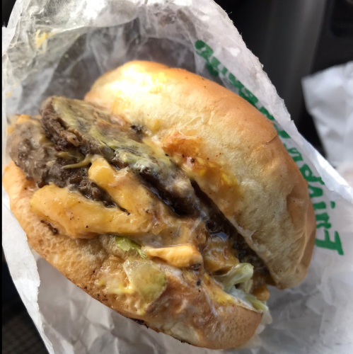 Close-up of a cheeseburger with melted cheese, lettuce, and two beef patties, wrapped in paper.