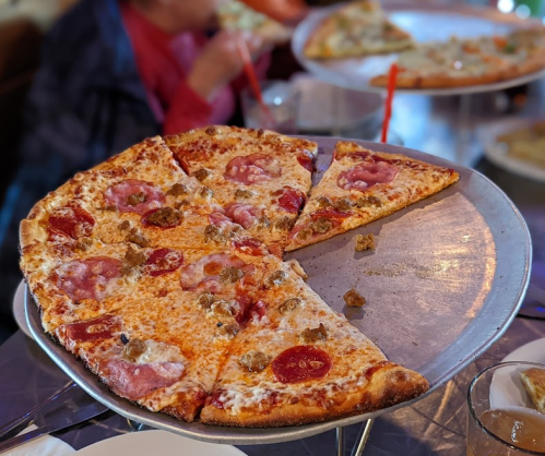 A large pizza on a metal tray, topped with pepperoni and sausage, with several slices removed.