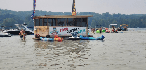 A floating rental shack on a lake with people kayaking and enjoying water activities in the background.