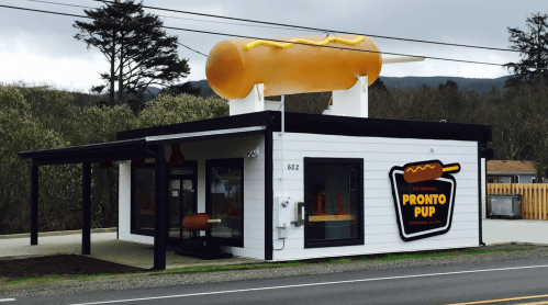 A building with a large hot dog sign on top, featuring the name "Pronto Pup" and a modern design.