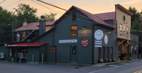 A rustic building with a red roof, featuring signs for "Francis Bar" and "Parking," set against a sunset sky.