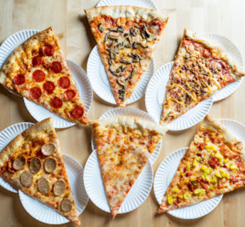 A variety of pizza slices on paper plates, including pepperoni, mushroom, cheese, and Hawaiian flavors.