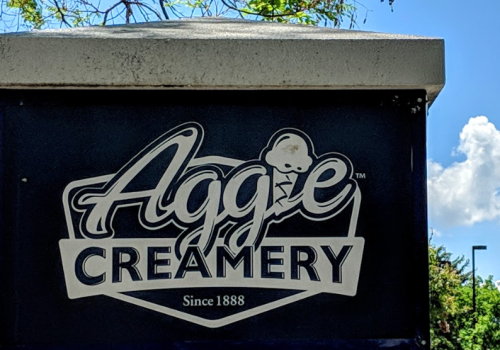 Sign for Aggie Creamery, established in 1888, featuring a logo with an ice cream cone against a blue sky.