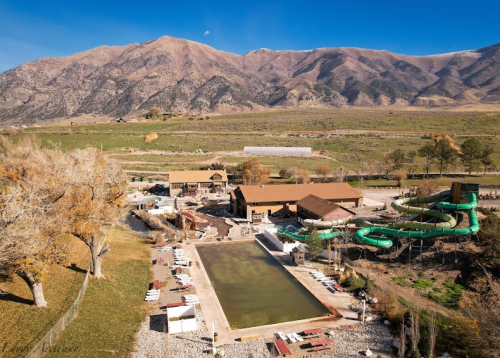 Aerial view of a resort with a pool, water slides, and mountains in the background under a clear blue sky.