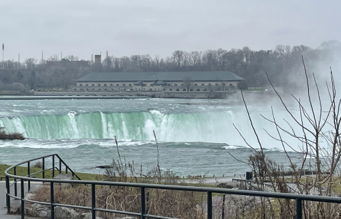 A view of Niagara Falls with mist rising, surrounded by trees and a building in the background.
