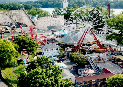 Aerial view of a vibrant amusement park featuring a ferris wheel, roller coaster, and various attractions surrounded by greenery.