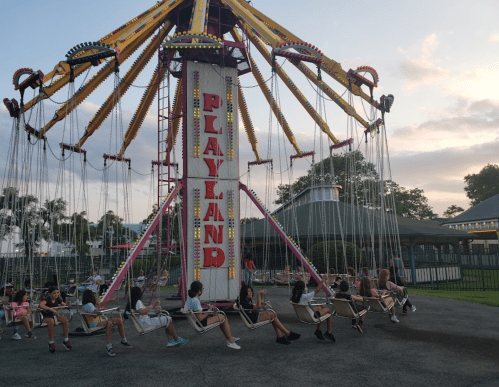 A colorful swing ride at an amusement park with children enjoying the evening sky in the background.