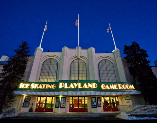 Exterior of a building at dusk, featuring signs for ice skating, Playland, and a game room, with flags on top.