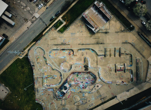 Aerial view of a graffiti-covered skatepark with various ramps and bowls, surrounded by streets and buildings.