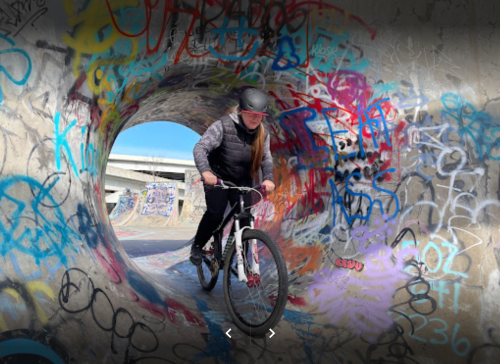 A person rides a bike through a graffiti-covered tunnel in a skate park.