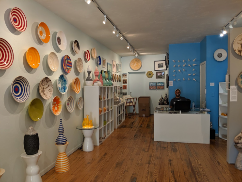 A bright art gallery featuring colorful ceramic plates on the walls and a smiling person at the reception desk.