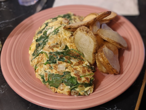 A pink plate with a spinach and cheese omelette alongside crispy potato wedges.
