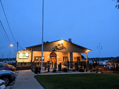 A cozy wooden restaurant exterior illuminated at dusk, with a welcoming entrance and nearby parked cars.