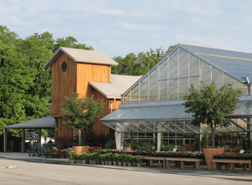 A wooden building and a large greenhouse surrounded by colorful flower beds on a sunny day.