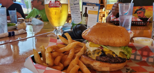 A juicy burger with lettuce, cheese, and condiments, served with fries and a beer in a casual dining setting.