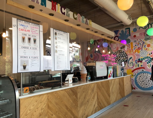 Colorful ice cream shop interior with a menu board, soft serve machine, and vibrant wall art.