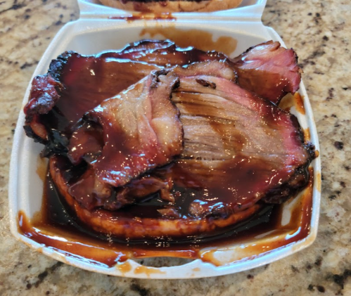 A container of sliced smoked meat covered in barbecue sauce, resting on a countertop.