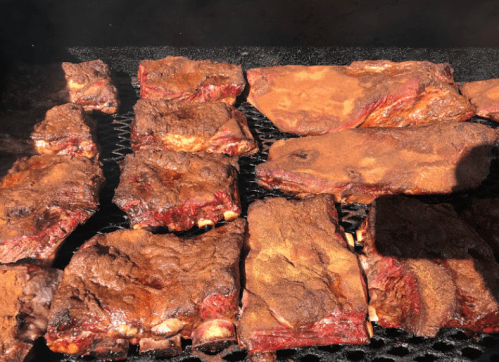 Close-up of seasoned ribs cooking on a grill, with a smoky texture and rich brown color.
