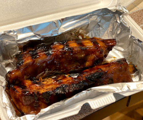 A takeout container with two glazed, grilled ribs resting on aluminum foil.